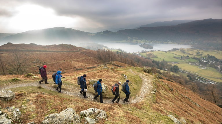 Walkers descending a path down the side of a fell towards the lake in Grasmere, Cumbria